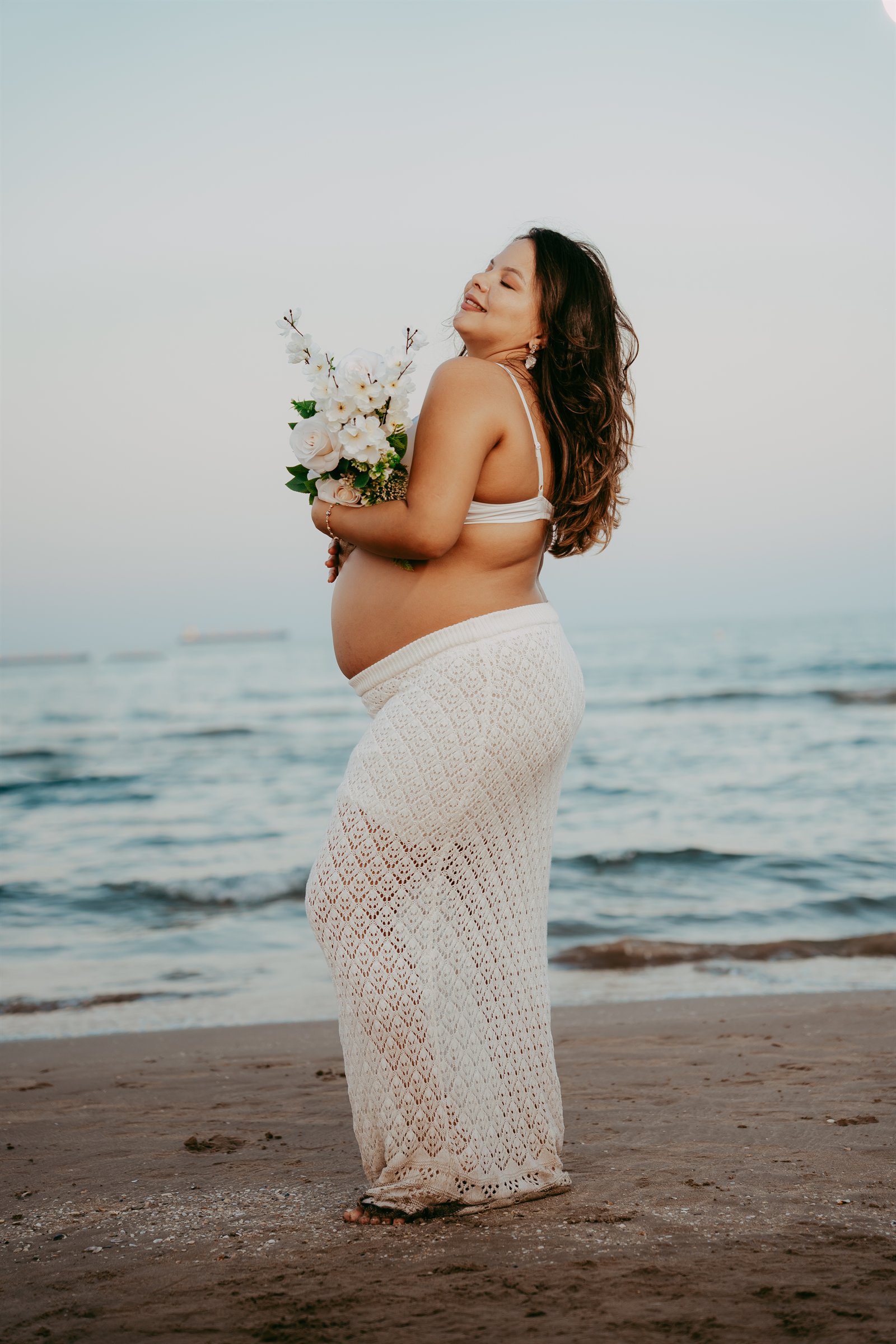 Virginia embarazada sostiene un ramo de flores junto al mar